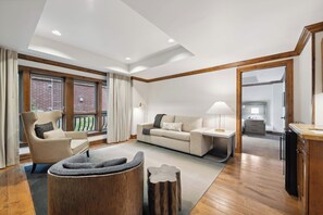 Ein geräumiges Wohnzimmer mit Sofa, Sessel und Couchtisch. Ein Holzkasten und eine Lampe stehen auf einem Beistelltisch.