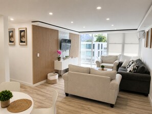 Ein modernes Wohnzimmer mit Sofa, Sessel und einem an der Wand befestigten Fernseher.