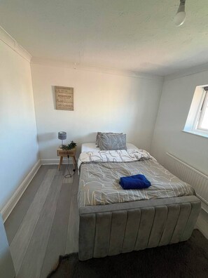 A bedroom with a bed, a bedside table with a lamp, a window, and a motivational quote on the wall. - The Urban Wharf - 4 Bedroom (London)