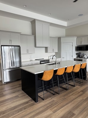 A modern kitchen with a central island, stainless steel appliances, and a seating area with chairs. - Superb 6-bedroom house on Lake of Egypt. The view is beautiful.  (Goreville)