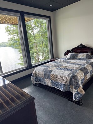 A bedroom with a large window, a bed with a patterned bedspread, and a dark wooden headboard. - Superb 6-bedroom house on Lake of Egypt. The view is beautiful.  (Goreville)