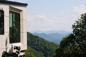 Un bâtiment moderne doté de grandes fenêtres, entouré de collines verdoyantes et avec des montagnes en toile de fond.