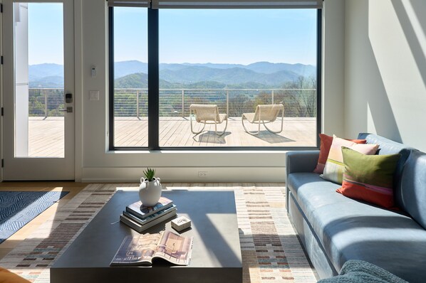 A modern living room with a large sliding glass door leading to a balcony with a view of mountains.