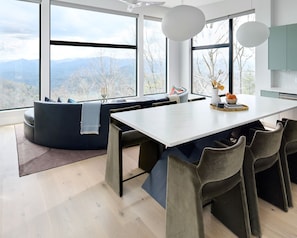 A modern dining area with a large table, chairs, and a view of mountains through large windows. - The Heartscape Collection | 3 Private Mountain Homes Near Asheville (Marshall)