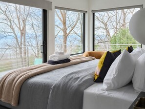 Une chambre d’hôtel avec un grand lit, une vue sur les arbres par les fenêtres et un balcon avec une balustrade.