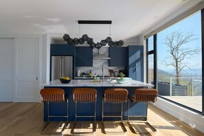 A modern kitchen with bar stools, a large window, and a view of the outdoors.