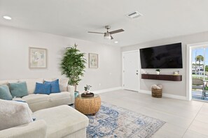 Una sala de estar moderna con un sofá, televisor, ventilador de techo y un ventanal grande.