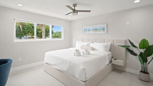 Ein Schlafzimmer mit Bett, Deckenventilator, Fenster mit Aussicht und einer Zimmerpflanze.