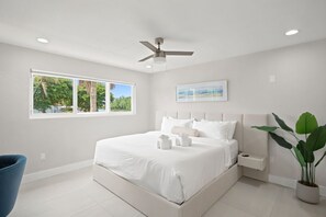 Ein Schlafzimmer mit Bett, Deckenventilator, Fenster mit Aussicht und einer Zimmerpflanze.