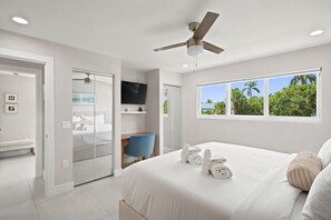 A hotel room with a bed, a ceiling fan, a TV, and a window with a view of palm trees. - Sanibel Arms C1 | Renovated Residence | Steps to Beach | Boat Dock (Sanibel)