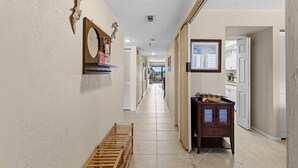 A hallway with a wooden bench, a mirror, and a cabinet with a tray. - Las Brisas 521 (New Smyrna Beach)