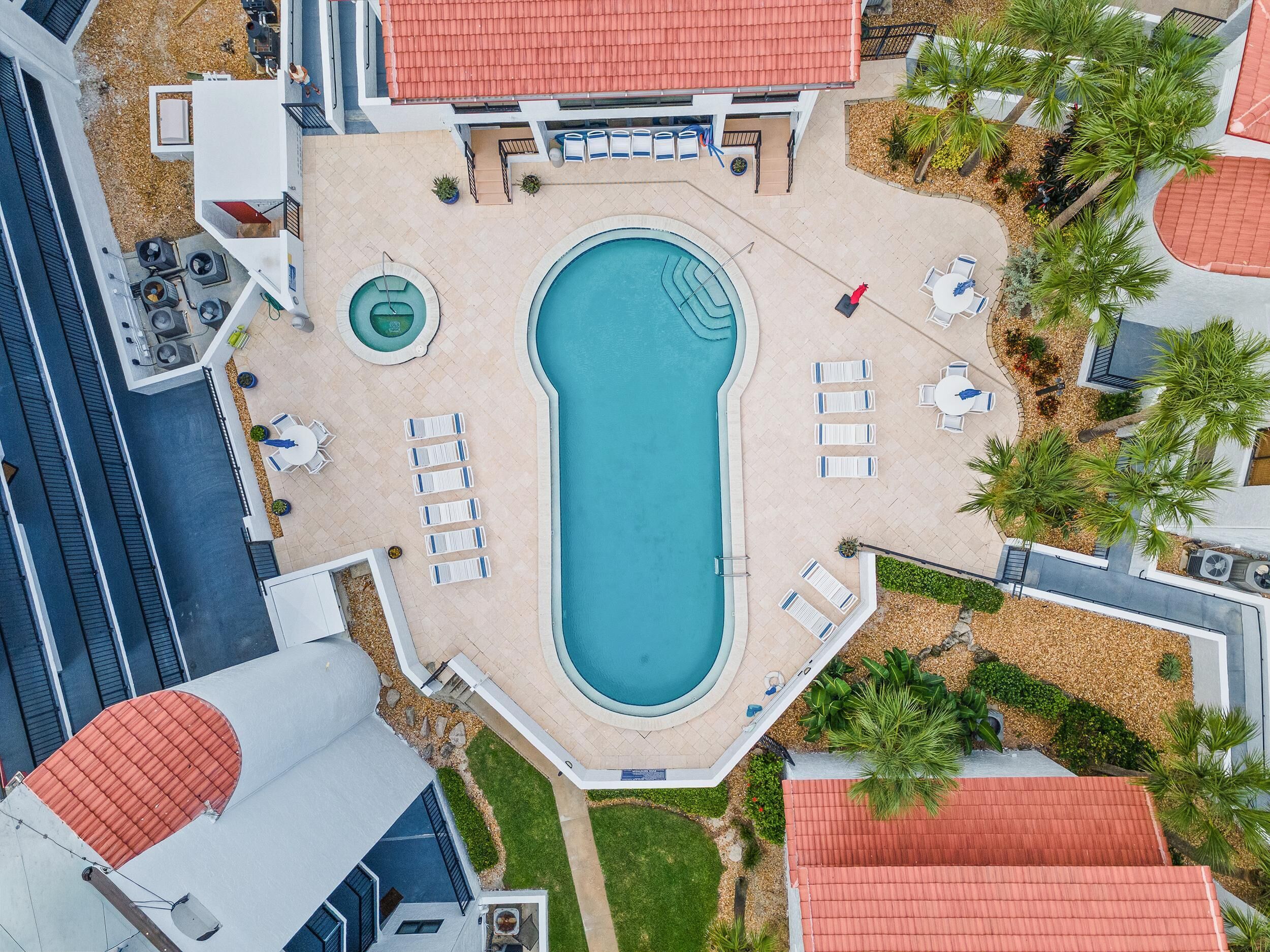 An aerial view of a hotel with a central swimming pool, lounge chairs, and a small hot tub.