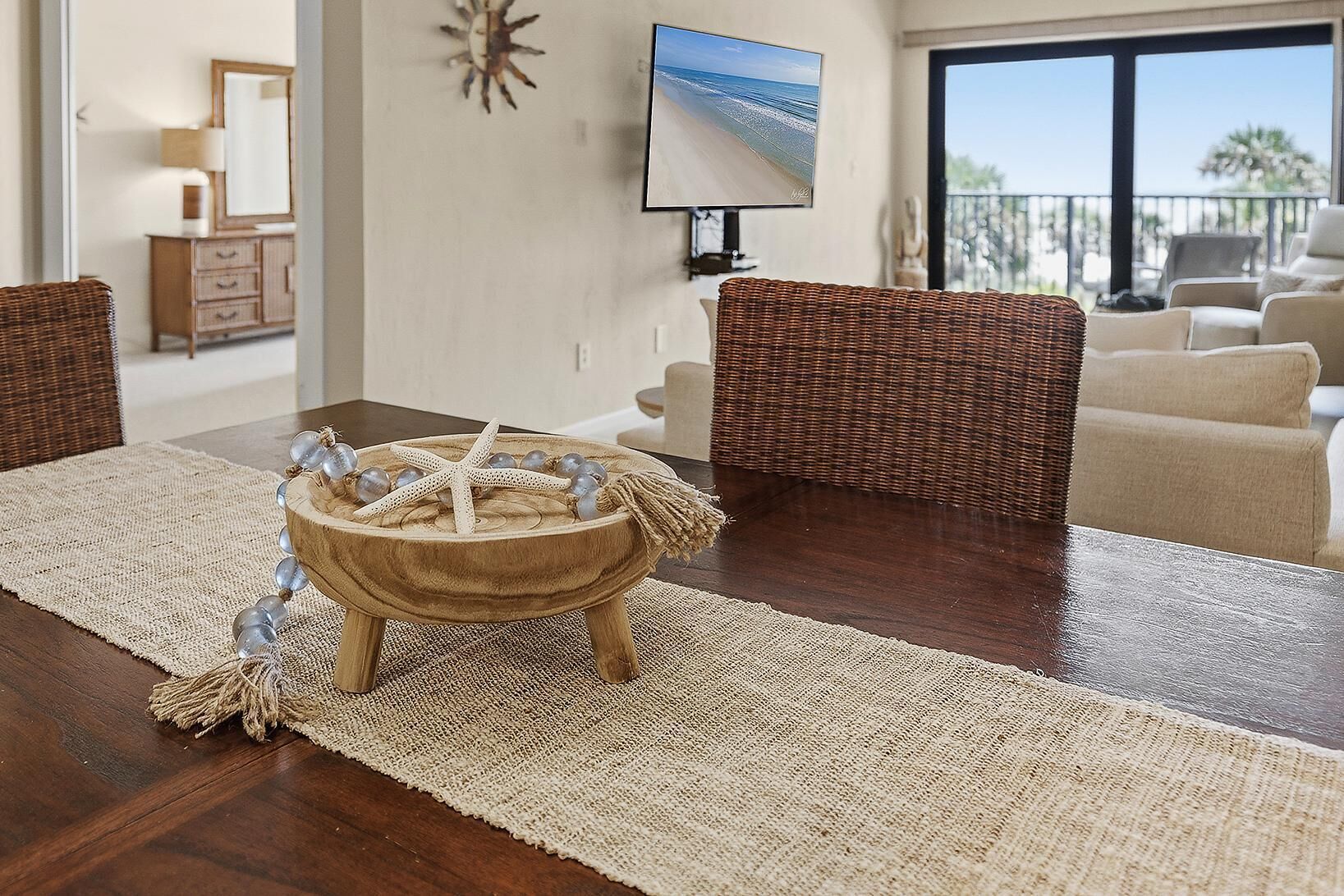 A living room with a round wooden table, wicker furniture, and a television mounted on the wall.