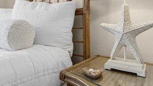 A bed with white bedding, a starfish decoration on a bedside table, and a bowl of seashells. - Las Brisas 521 (New Smyrna Beach)