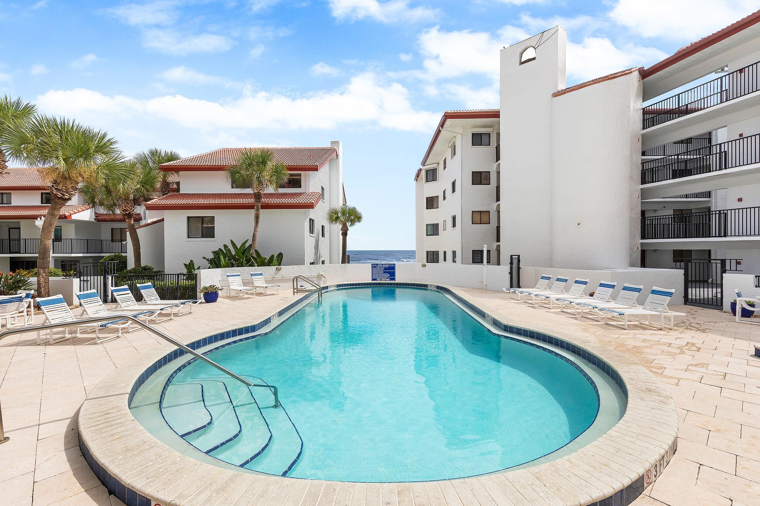 Una piscina con sillas de descanso y palmeras, rodeada de edificios con balcones.