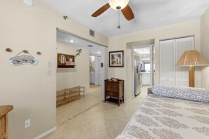 Une chambre à coucher comprenant un lit, un ventilateur de plafond, une lampe, une commode et une porte donnant sur une autre pièce.