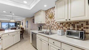 A modern kitchen with white cabinetry, a tiled backsplash, a built-in dishwasher, and a toaster. - Las Brisas 521 (New Smyrna Beach)