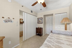 A bedroom with a bed, a nightstand, a dresser, a ceiling fan, and a door leading to another room. - Las Brisas 521 (New Smyrna Beach)