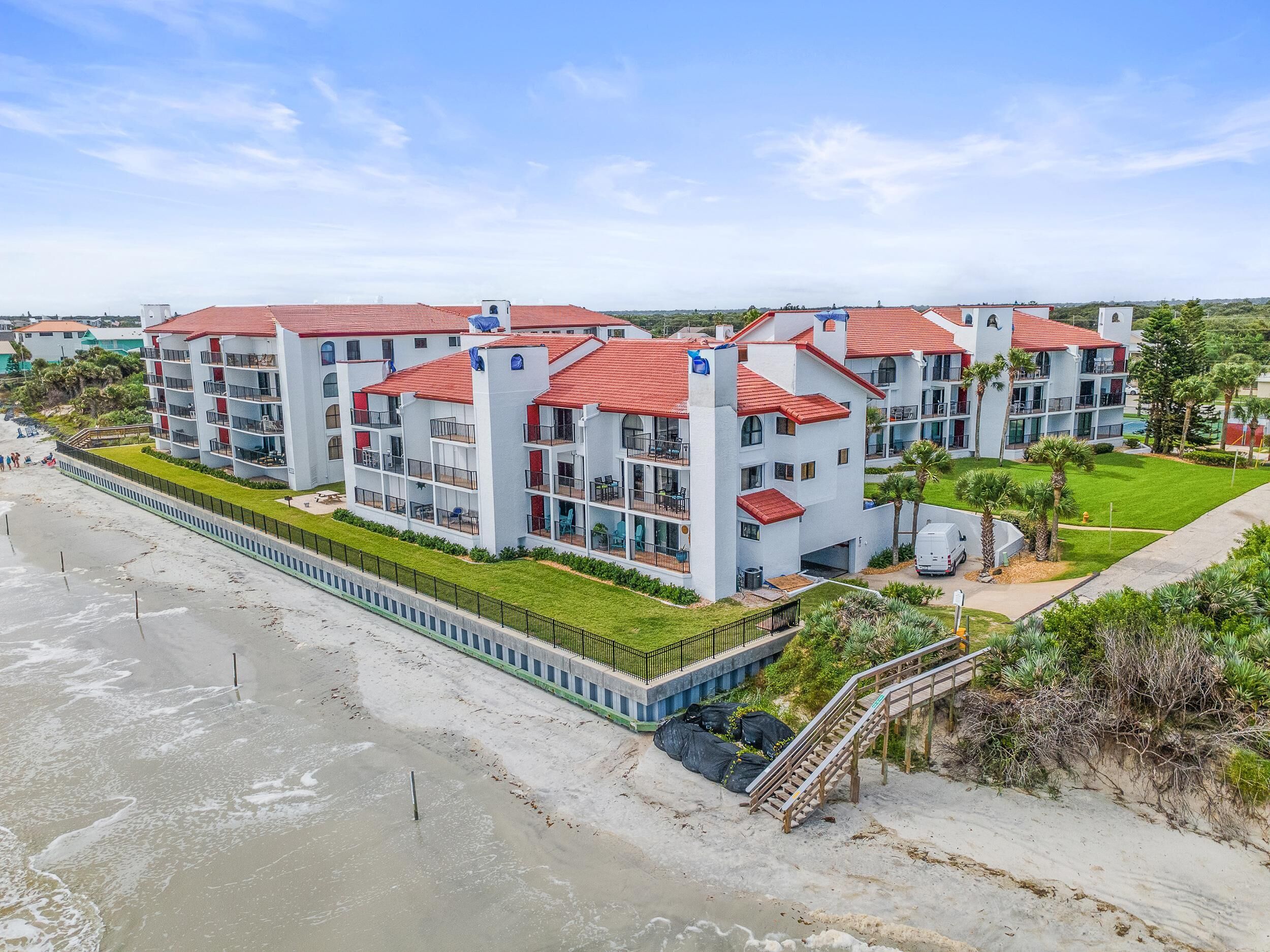 Ein Hotel direkt am Strand mit mehreren Etagen, roten Ziegeldächern und Balkonen.