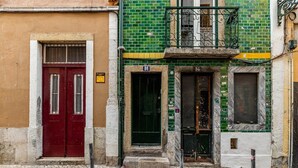 Una fila di edifici con stili architettonici diversi, tra cui un portone rosso, una facciata con tegole verdi e un balcone con ringhiere in ferro.