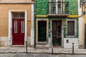 Eine Reihe von Gebäuden mit unterschiedlichen Architekturstilen, darunter eine rote Tür, eine grün gekachelte Fassade und ein Balkon mit Eisenverzierungen.