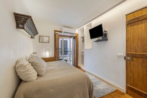 A bedroom with a bed, a television mounted on the wall, and a wooden door. - Apartment 'Sweet Rose Bairro Alto' with Balcony and Wi-Fi (Lisbon)
