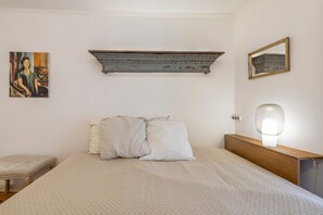 A bedroom with a bed, pillows, a nightstand, a lamp, a mirror, and a painting on the wall. - Apartment 'Sweet Rose Bairro Alto' with Balcony and Wi-Fi (Lisbon)