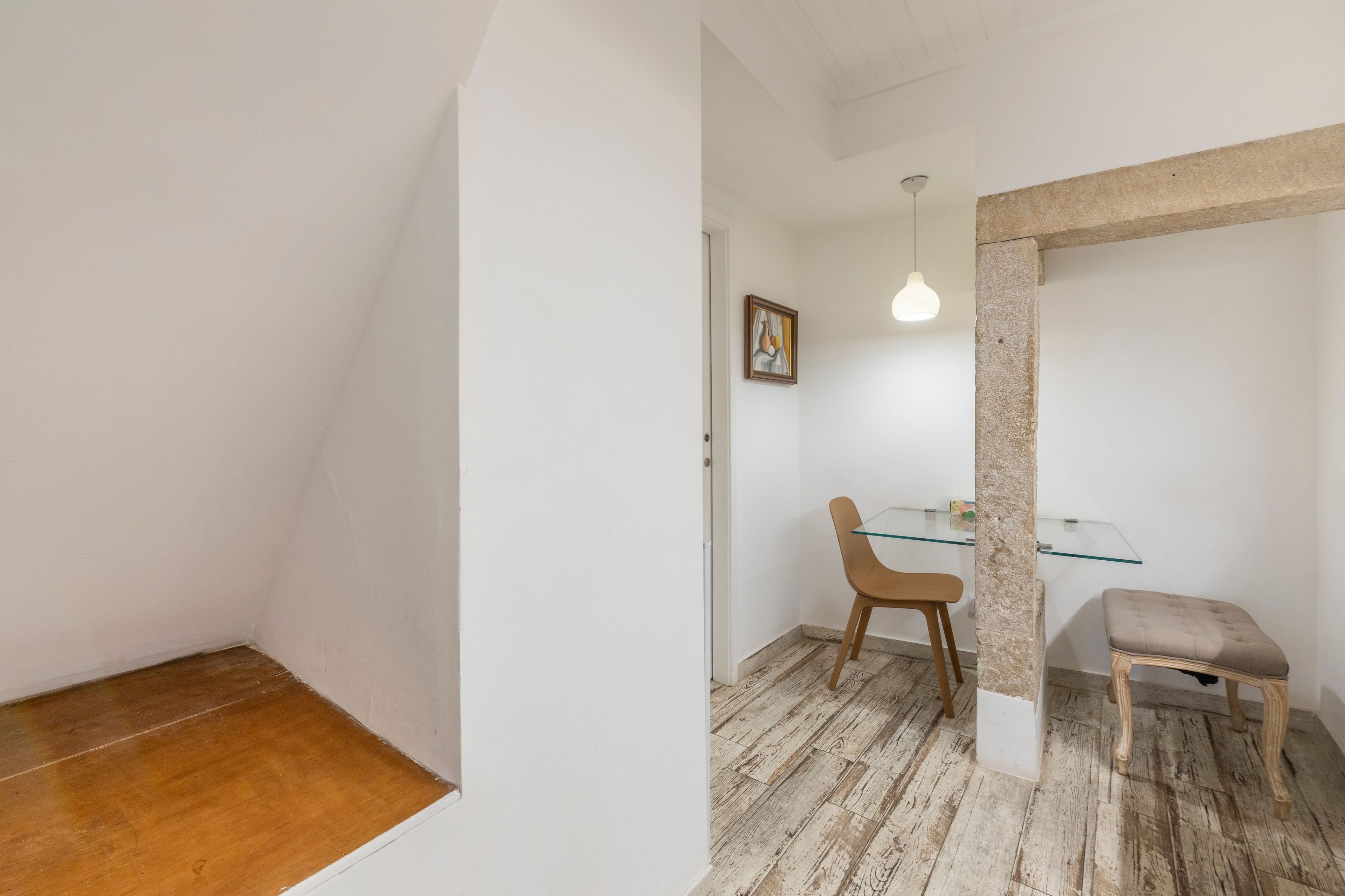 A room with a wooden floor, a glass table, a wooden chair, a cushioned bench, and a hanging light fixture.