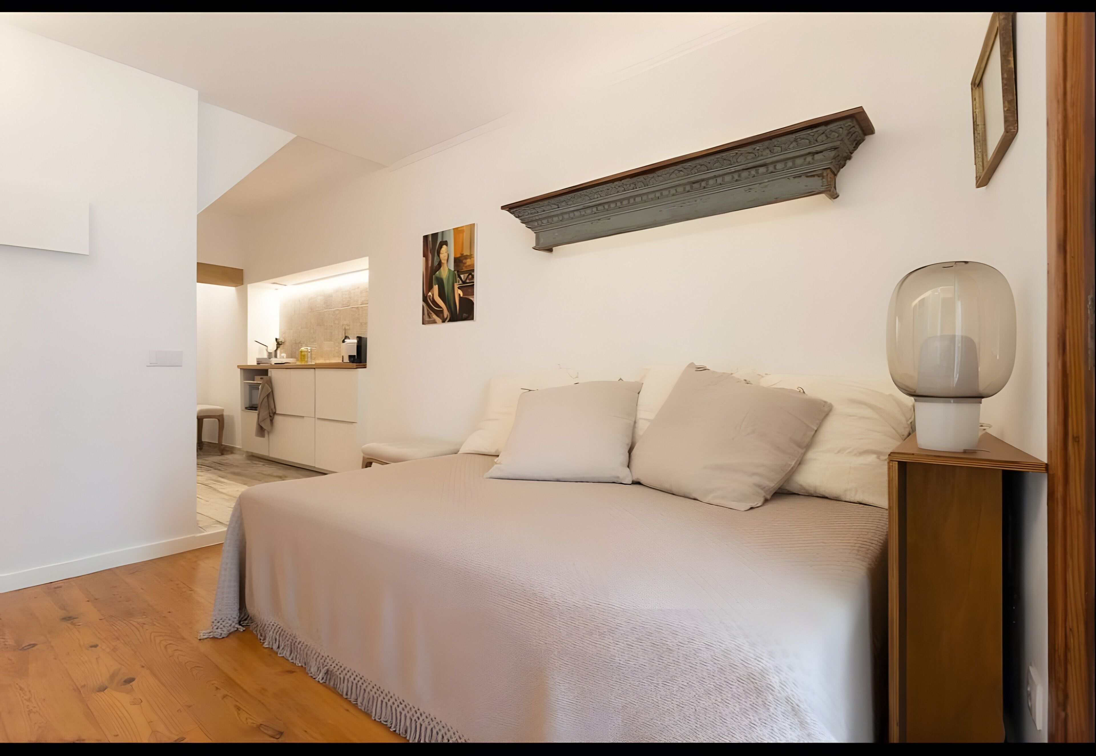A bedroom with a bed, a bedside table, a lamp, and a wall-mounted shelf.