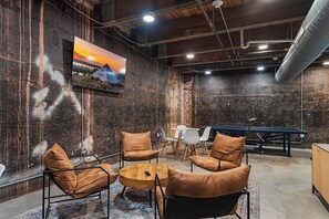 Een moderne zithoek met een ronde houten tafel, lederen fauteuils en een aan de muur bevestigde televisie.