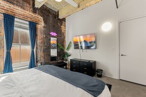Een slaapkamer met een bed, een dressoir, een spiegel, een televisie en een deur.