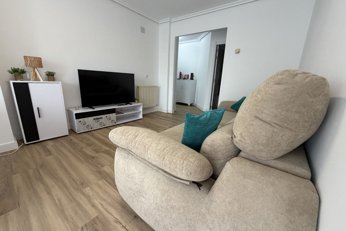 Uma sala de estar com um sofá bege, uma televisão de tela plana e um armário branco.