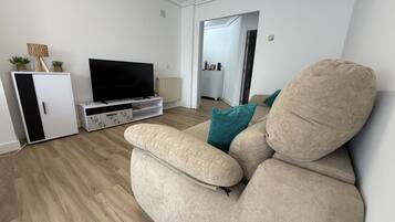 Uma sala de estar com um sofá bege, uma televisão de tela plana e um armário branco.