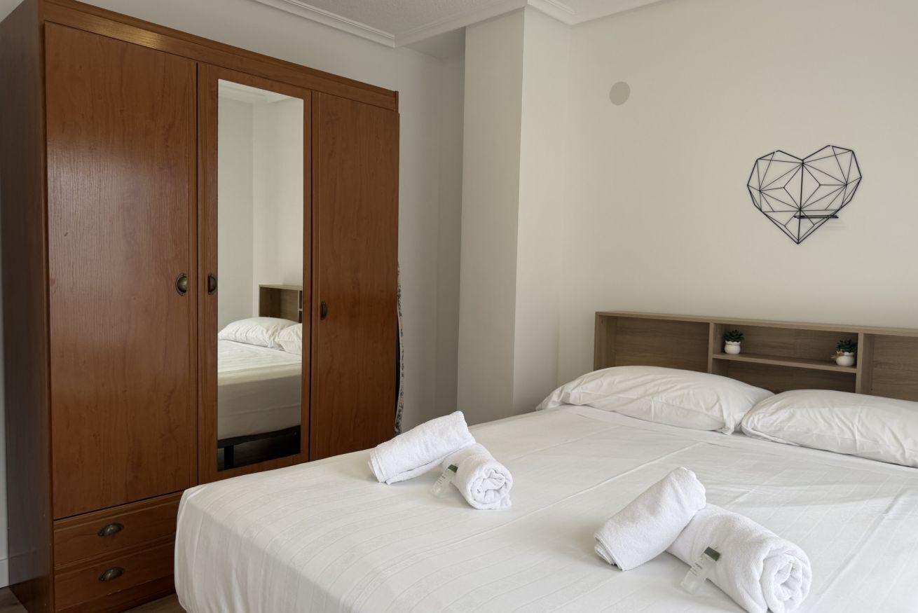 Una habitación de hotel con un amplio armario de madera, una cama con ropa blanca y una obra de arte geométrica en la pared.