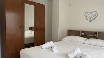 Una habitación de hotel con un amplio armario de madera, una cama con ropa blanca y una obra de arte geométrica en la pared.
