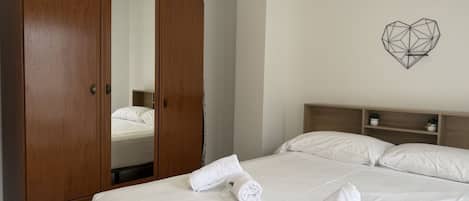 A hotel room with a large wooden wardrobe, a bed with white linens, and a geometric wall art piece.