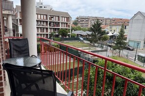 A balcony with a glass table and chairs, overlooking a residential area with multi-story buildings and a street.