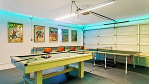 Una habitación con dos mesas de fútbolín, una mesa de billar y cuatro sillas naranjas.