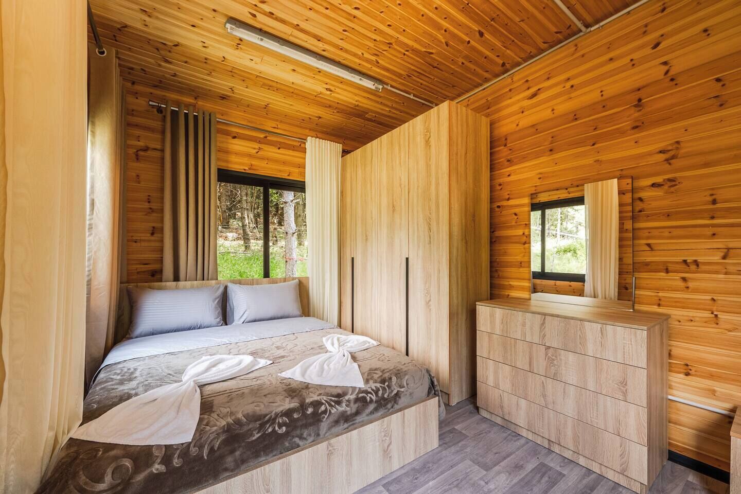 A wooden room with a bed, a dresser, and a window.