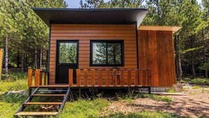 A cabin with a wooden exterior, two windows, a door, and a small porch with a wooden bench.