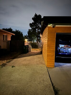 A residential garage with a wooden exterior, a driveway leading to the garage, and a vehicle inside. - Cozy West Elm Stay Near Expo & Mountain Fun (Sandy)