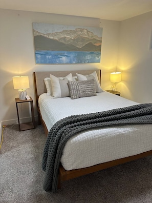A bedroom with a bed, two bedside lamps, a painting above the bed, and a carpeted floor. - Cozy West Elm Stay Near Expo & Mountain Fun (Sandy)