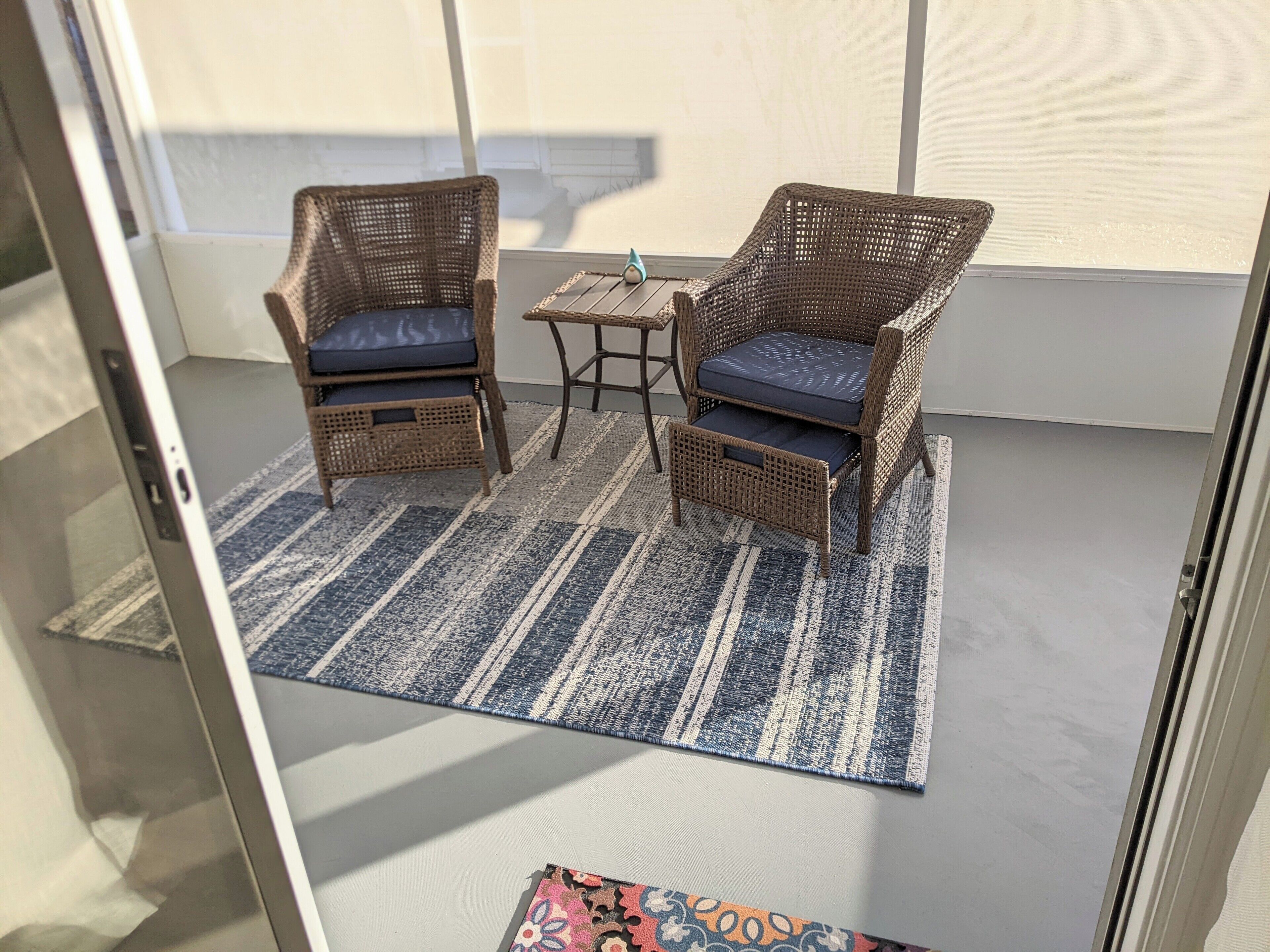 Una habitación con dos sillones de mimbre con cojines, una mesita y un tapete a rayas.