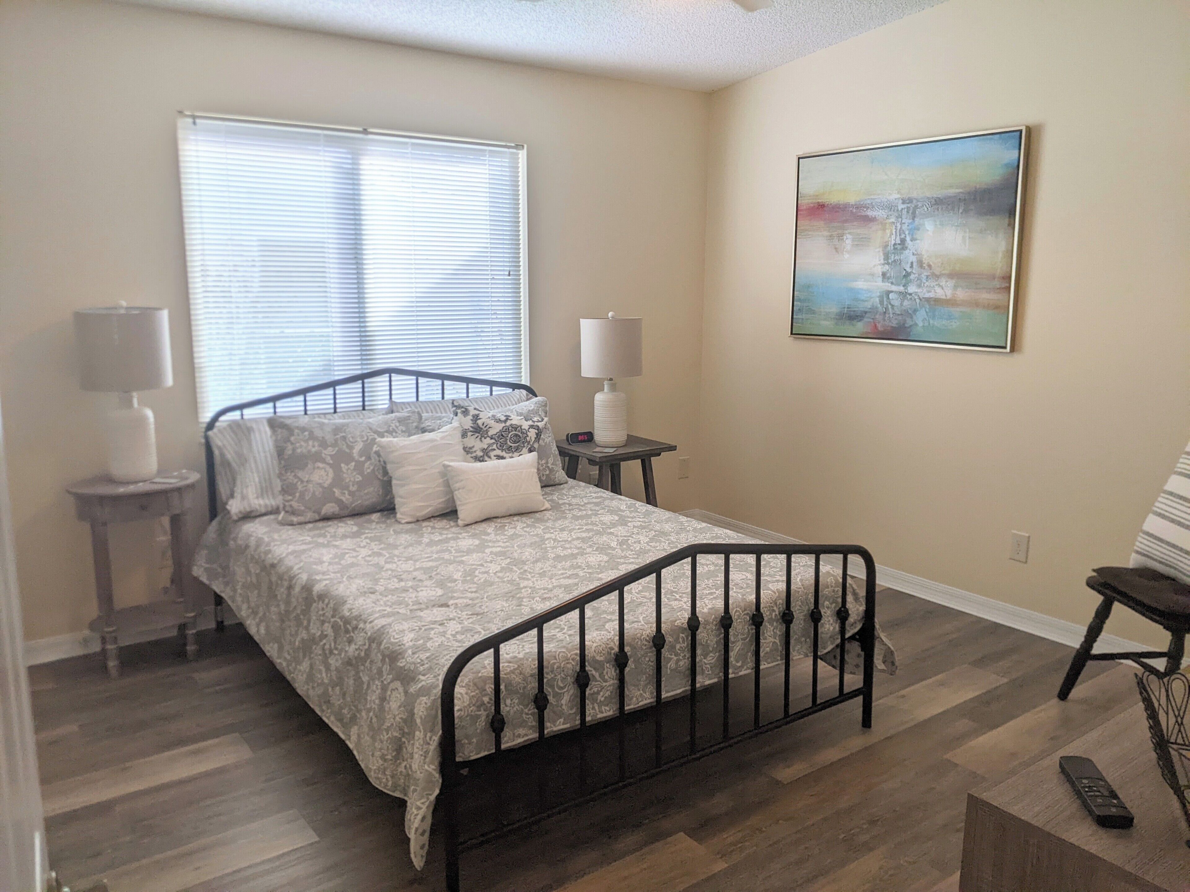 A bedroom with a bed, two bedside tables, a lamp, a painting, and a chair.