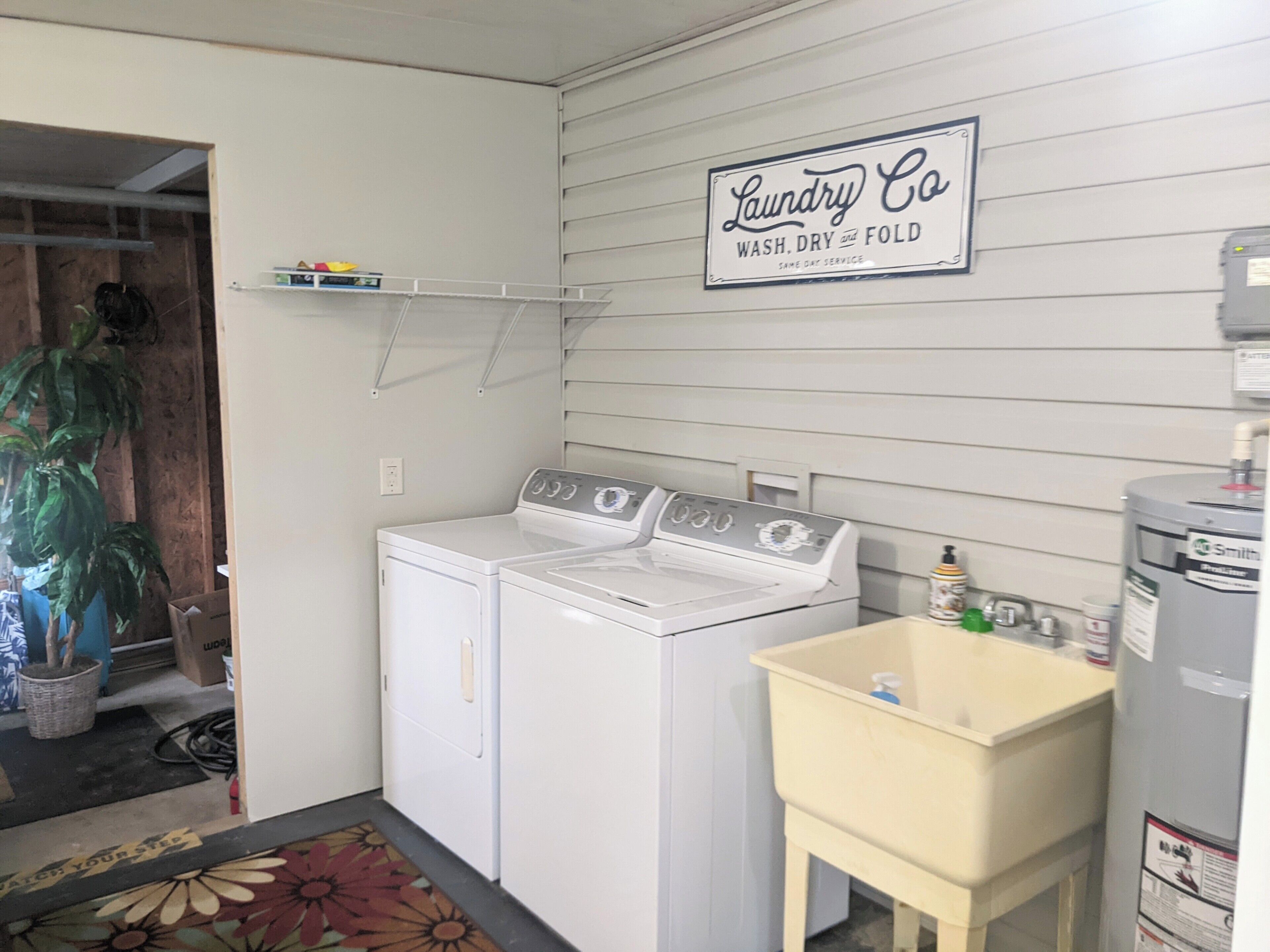 Ein Waschraum mit einem Schild, das 'Laundry Co Wash, Dry and Fold' zeigt, sowie ein Waschbecken mit Reinigungsmitteln.