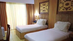 A hotel room with two single beds, a nightstand with a lamp, a wooden headboard, and a window with curtains. - Hotel Mazafran (Algiers)