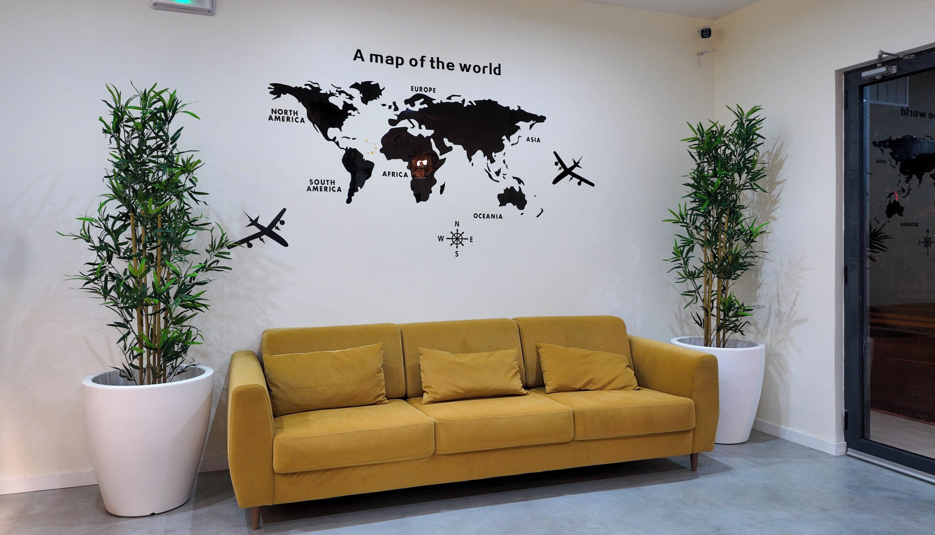 Une pièce décorée avec une grande carte du monde au mur, un canapé de couleur moutarde et deux plantes en pot.