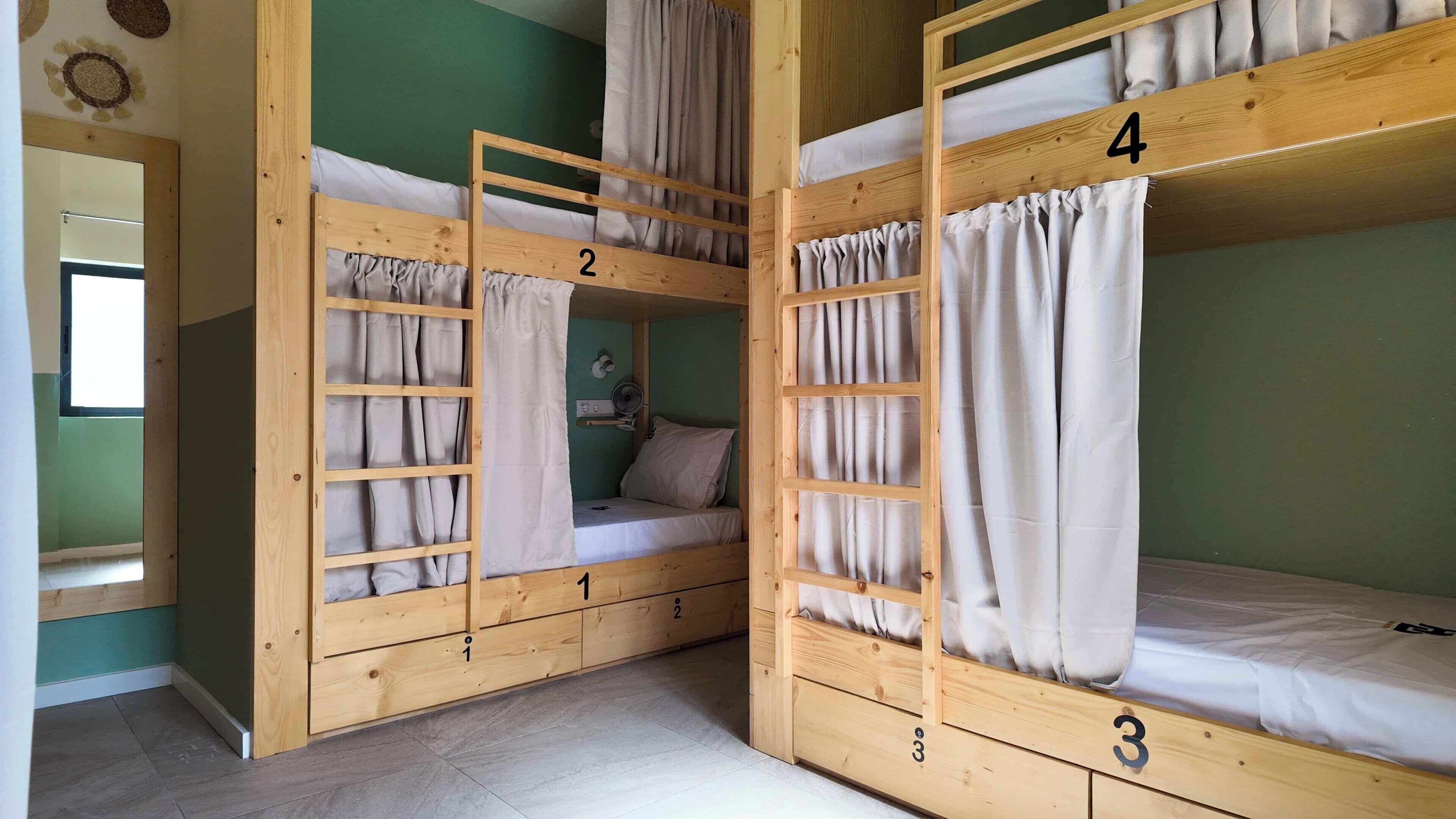 Een kamer met vier stapelbedden, elk voorzien van een nummer van 1 tot 4, en een klein nachtkastje met een lamp.