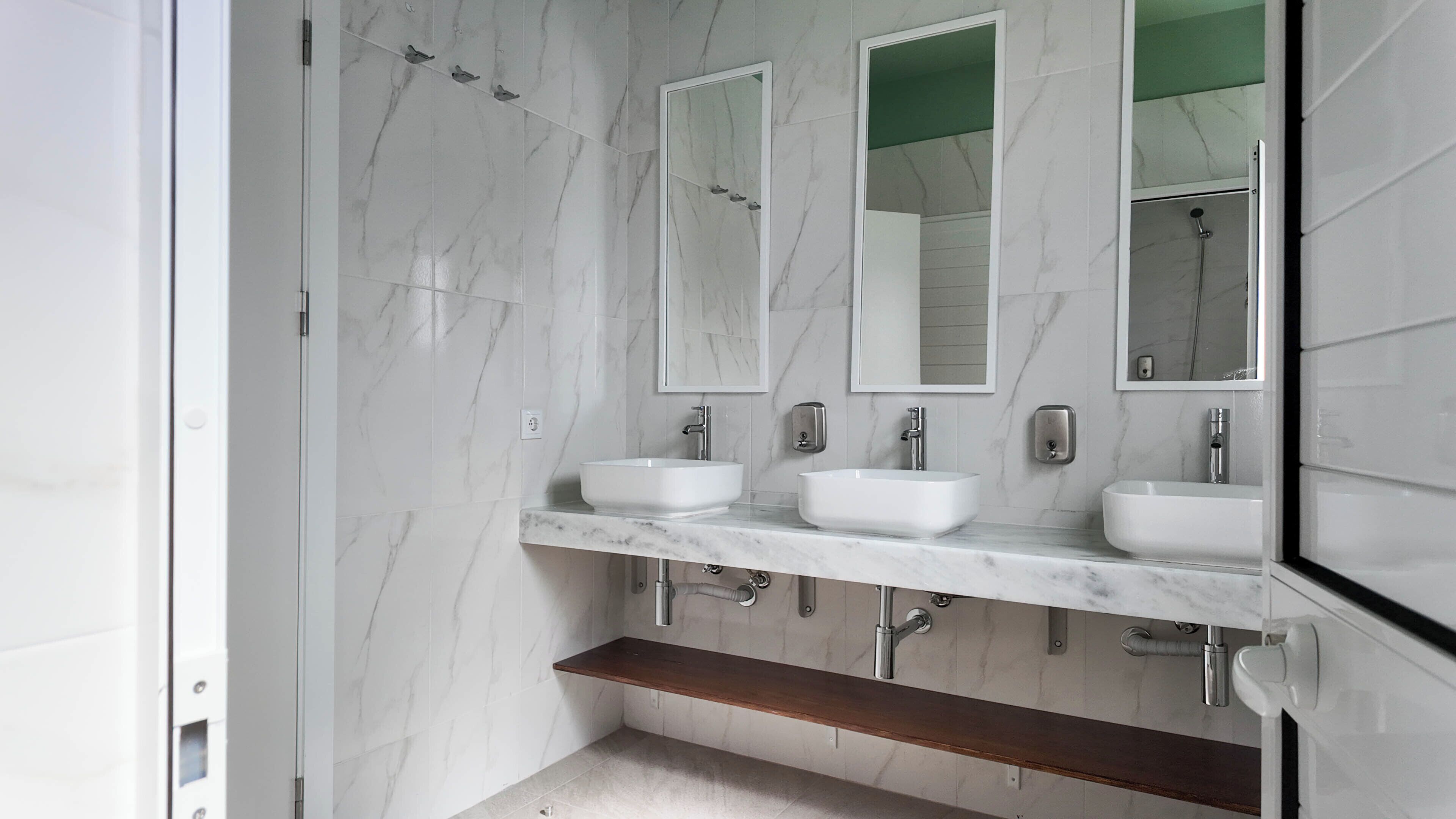 A modern bathroom with three sinks, two mirrors, and a shower.
