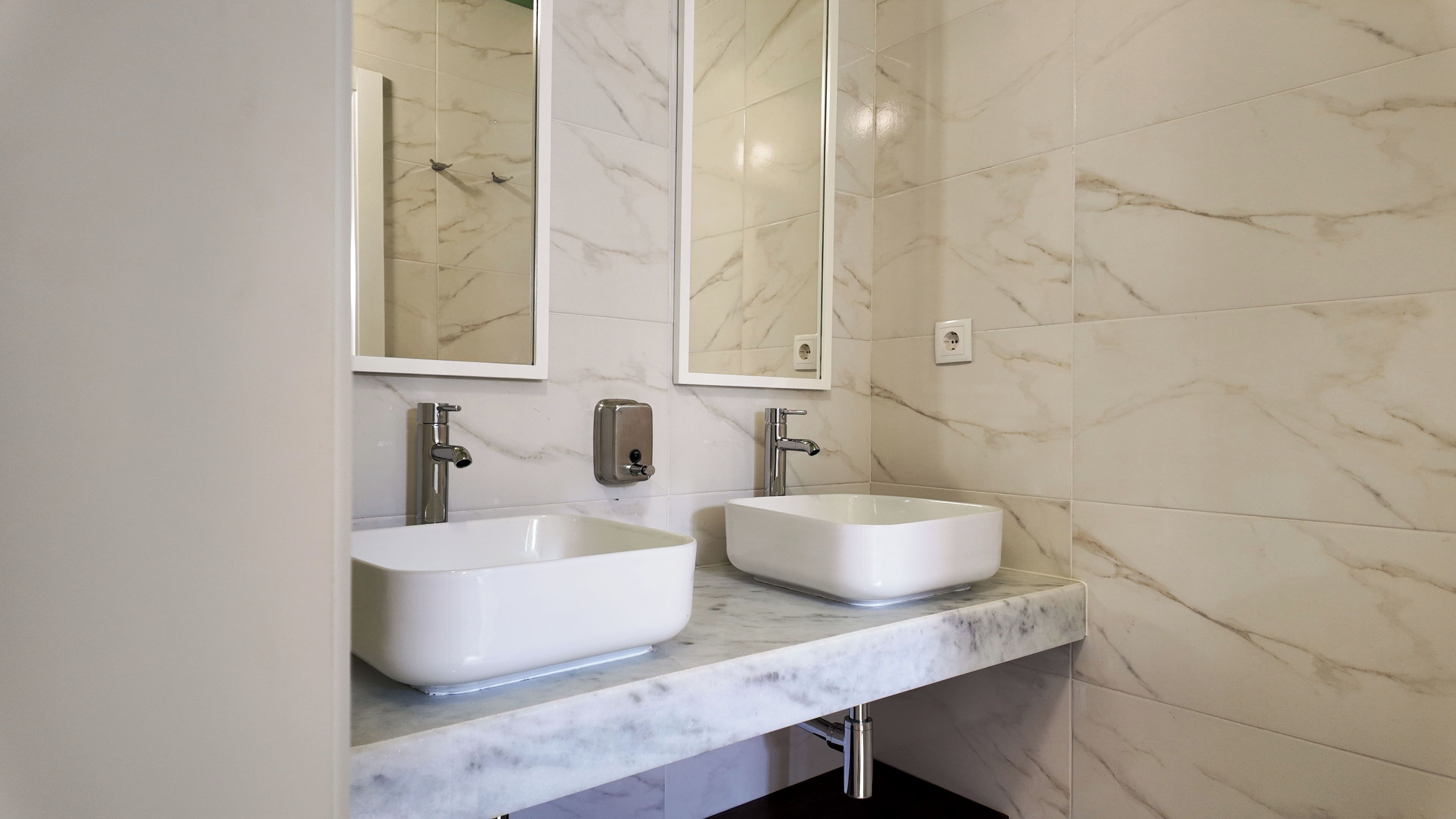 A bathroom with two sinks, a mirror, and a marble wall.